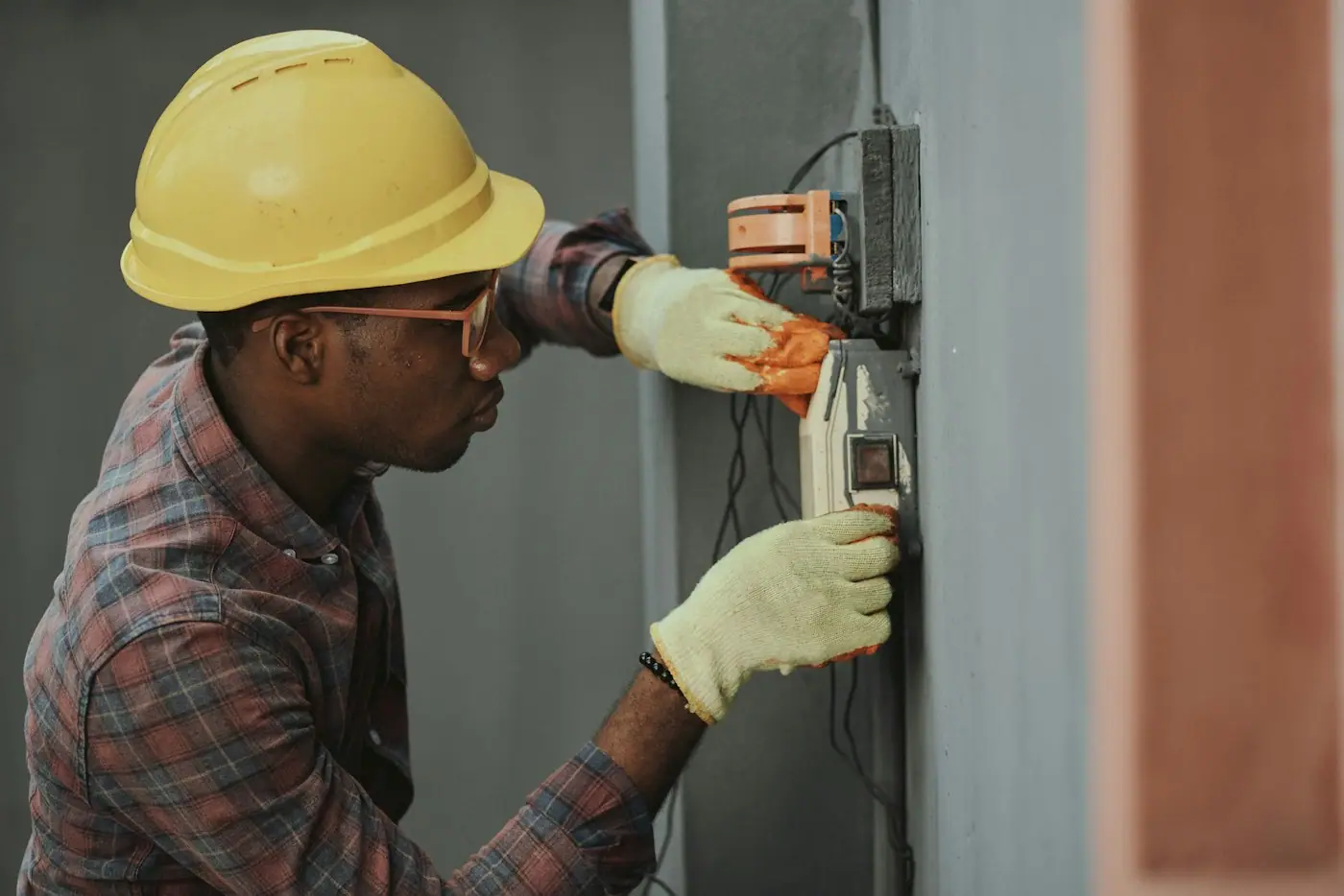 Technician in a hard hat and gloves working on an electrical panel