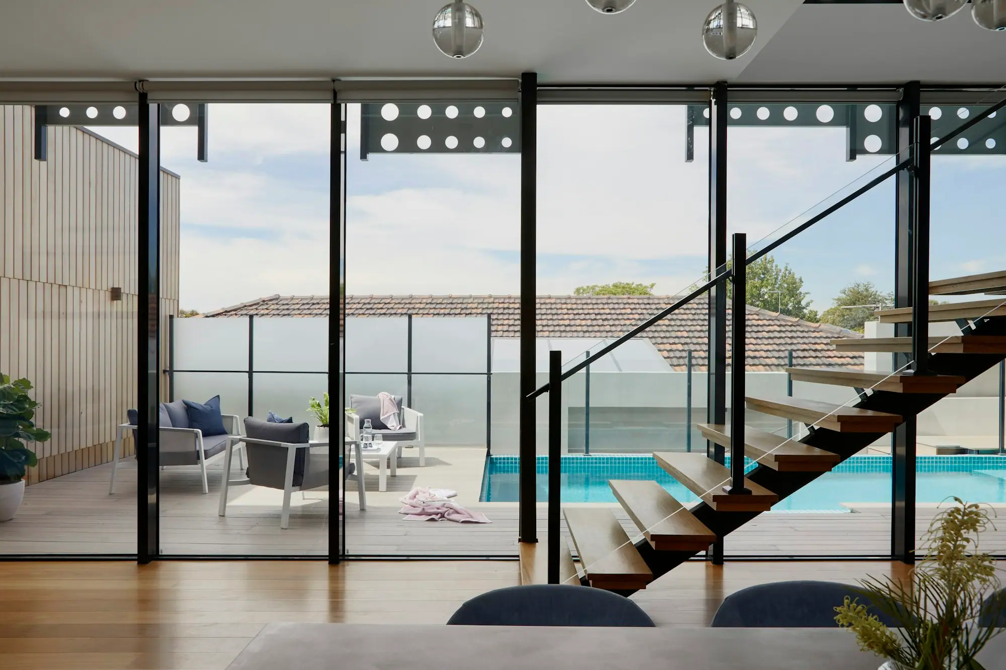 Double-height living space with a floating timber staircase and glass walls